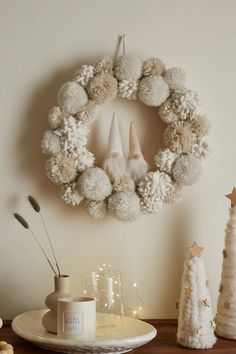 a christmas wreath with pom - poms hanging on the wall next to candles