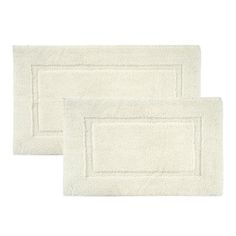 two white bath mats on top of each other, one with a border in the middle