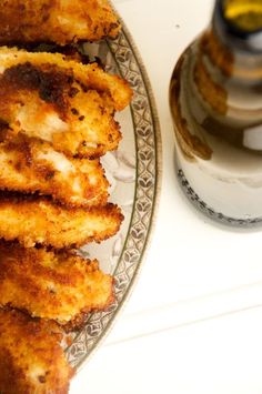 some fried food on a plate next to a bottle of oil and a glass container