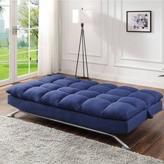 a blue futon sofa bed sitting on top of a wooden floor next to a window