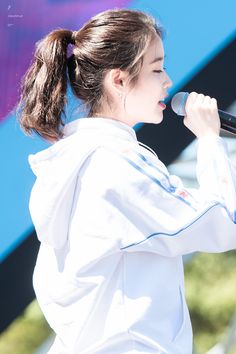 a young woman holding a microphone in her right hand and wearing a white shirt with blue piping on it