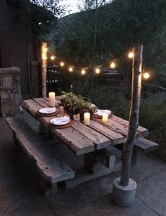 a wooden table topped with plates and lit candles next to a fire pit in the middle of a yard