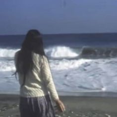 a woman standing on top of a beach next to the ocean with waves coming in