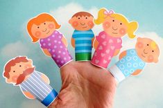 a hand holding several paper dolls in the shape of children's faces, with clouds behind them