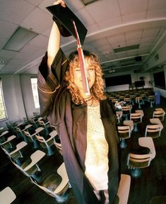 a woman in a graduation cap and gown holds her diploma above her head while standing in front of rows of empty chairs