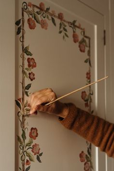 a woman holding a stick in front of a floral wallpapered door with flowers on it