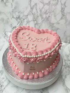 a pink heart shaped cake sitting on top of a white table next to a marble counter