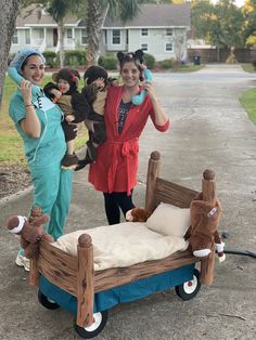 two women in costumes standing next to a bed with teddy bears on it and one woman holding up her cell phone