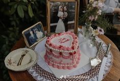 a heart shaped cake sitting on top of a table next to two pictures and flowers