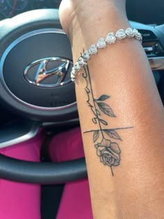 a woman's arm with a rose tattoo on it and a steering wheel behind her