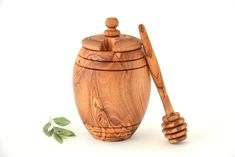 a wooden honey jar with a spoon next to it on a white surface and a green leaf