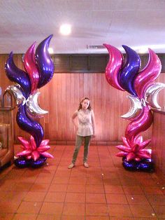 a woman standing in front of two purple and silver flowers with balloons attached to them