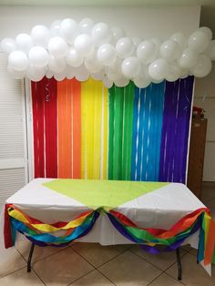 a rainbow themed party table with balloons and streamers on the wall in front of it