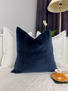 a blue pillow sitting on top of a bed next to a cup and saucer