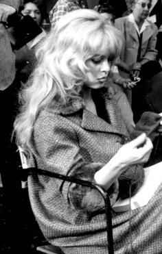 a black and white photo of a woman sitting in a chair looking at her cell phone