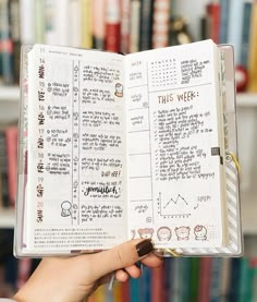 someone is holding an open planner in front of a bookshelf full of books