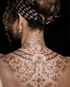 the back of a woman's neck is adorned with intricate designs and feathers on it