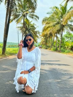 a woman kneeling down on the side of a road with palm trees in the background