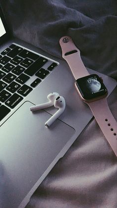 an apple watch and ear buds are on the table next to a laptop computer that is open