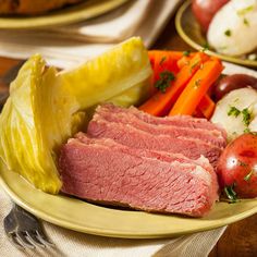 corned beef with carrots, potatoes and tomatoes on a yellow plate next to silverware