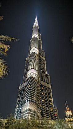 the burj building is lit up at night with palm trees in foreground