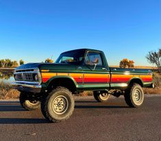 a green truck with red, yellow and orange stripes parked on the side of the road