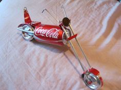 a toy airplane made out of coca - cola cans is on a bed with white sheets