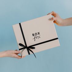 two hands holding a white box with a black ribbon around it and the word box for