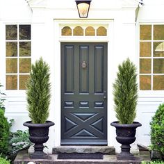 two large planters are in front of the door to a white house with black trim