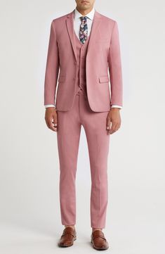 a man in a pink suit and tie is standing with his hands in his pockets