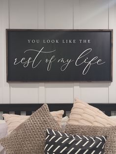 a bed topped with lots of pillows next to a sign that says you look like the rest of my life