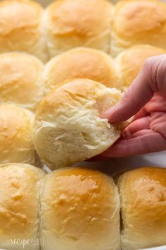 a person picking up a piece of bread from a baking pan filled with buns