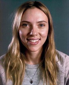 a woman with long blonde hair smiles at the camera while wearing a gray shirt and silver necklace