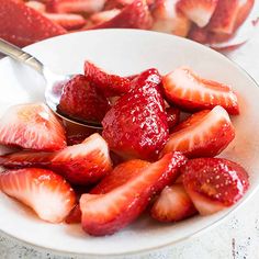 strawberries in a white bowl with a spoon on the side and another plate full of strawberries