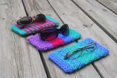 three crocheted glasses cases sitting on top of a wooden table next to sunglasses