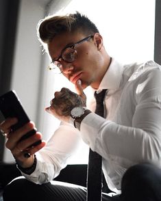 a man wearing glasses and a white shirt is looking at his cell phone while sitting in a chair