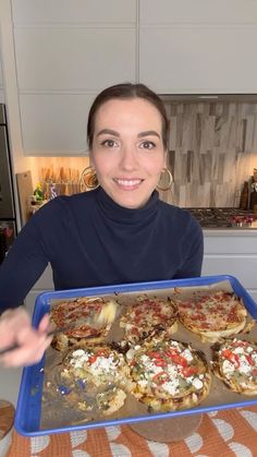 a woman holding up a tray of pizzas