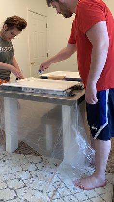 a man and woman standing in front of a table that is being wrapped up with plastic