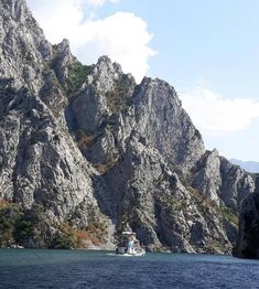 there is a boat that is in the water near some mountains and trees on the side of the mountain