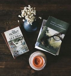 two books and a vase with flowers on a wooden table next to a cup of tea