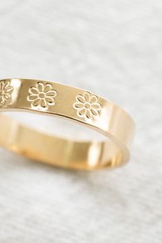 a yellow gold ring with flowers engraved on the side, sitting on a white surface