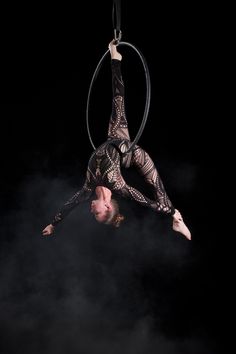 a woman is doing aerial acrobatics in the air on a hoop above her head