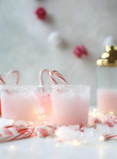 three glasses filled with pink liquid and candy canes on top of snow covered ground