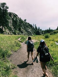 two women walking down a dirt road in the mountains with backpacks on their backs