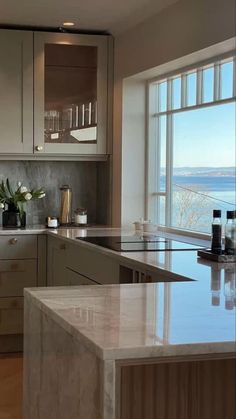 a large kitchen with marble counter tops and white cabinets, along with an ocean view