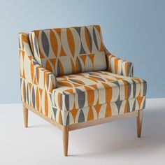 an orange and gray patterned chair sitting on top of a white floor next to a blue wall