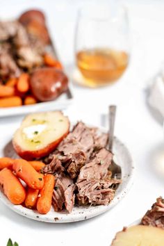 two plates with meat, carrots and potatoes on them next to some wine glasses