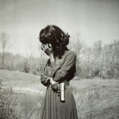 a woman standing in a field with her hand on her face while holding a bottle