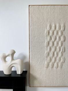 a white vase sitting on top of a black table next to a wall mounted art piece