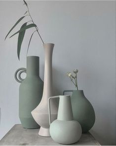 three vases are sitting on a table next to each other, one has a plant in it